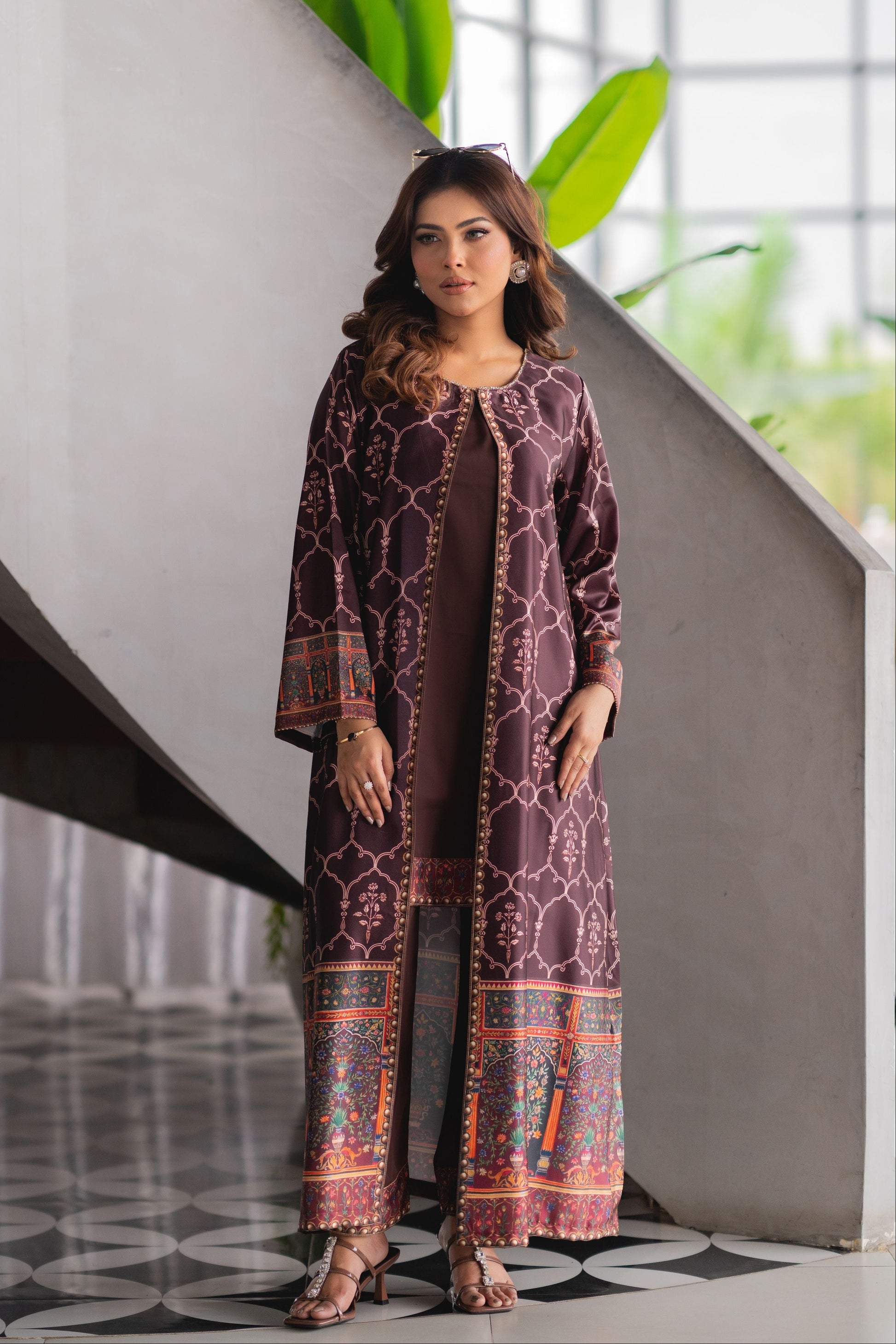 Woman wearing a patterned outfit standing indoors with plants in the background