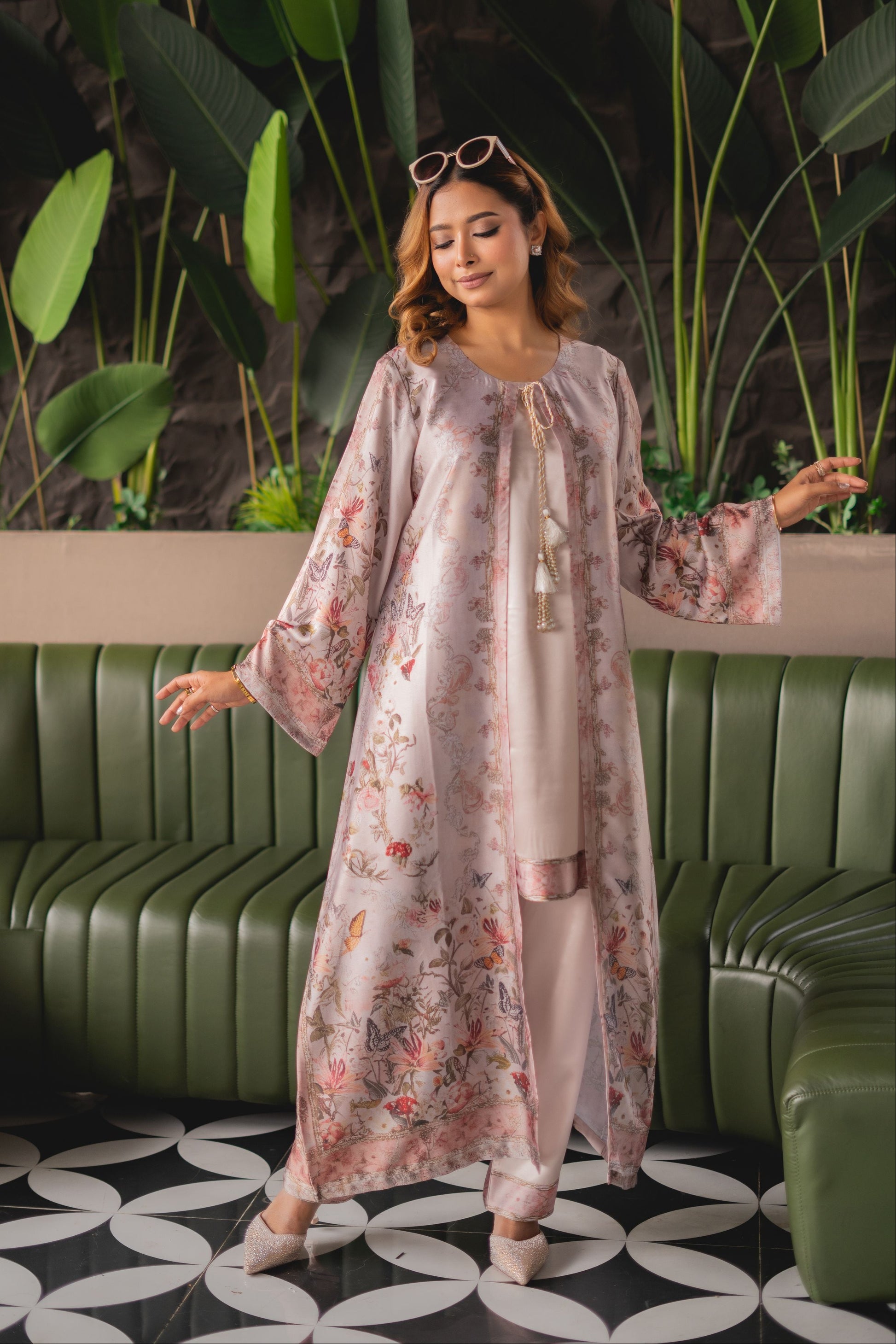 Woman in a floral dress standing in a stylish interior setting with green plants and a green couch.