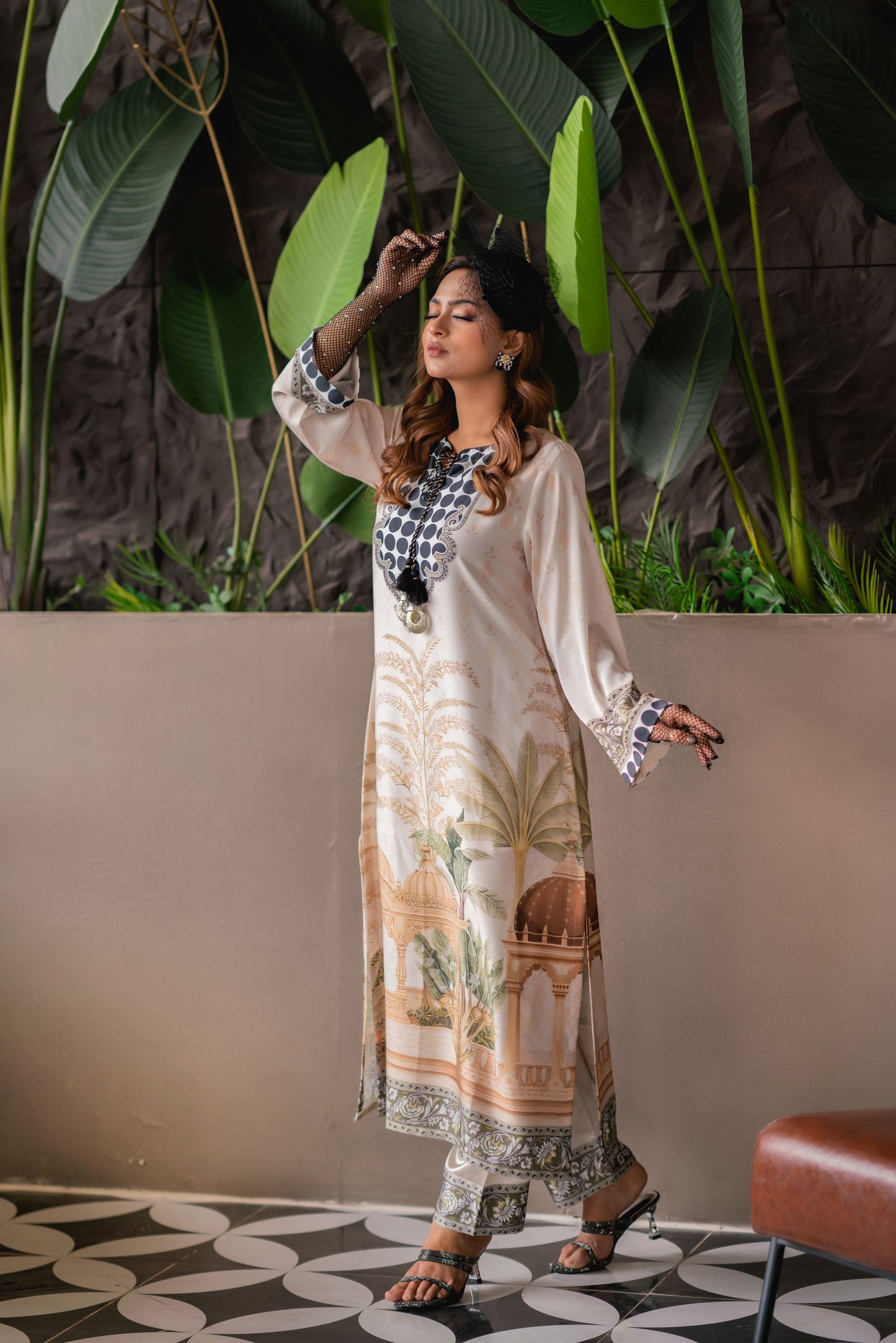 Woman in a patterned dress standing in a room with plants and a couch.