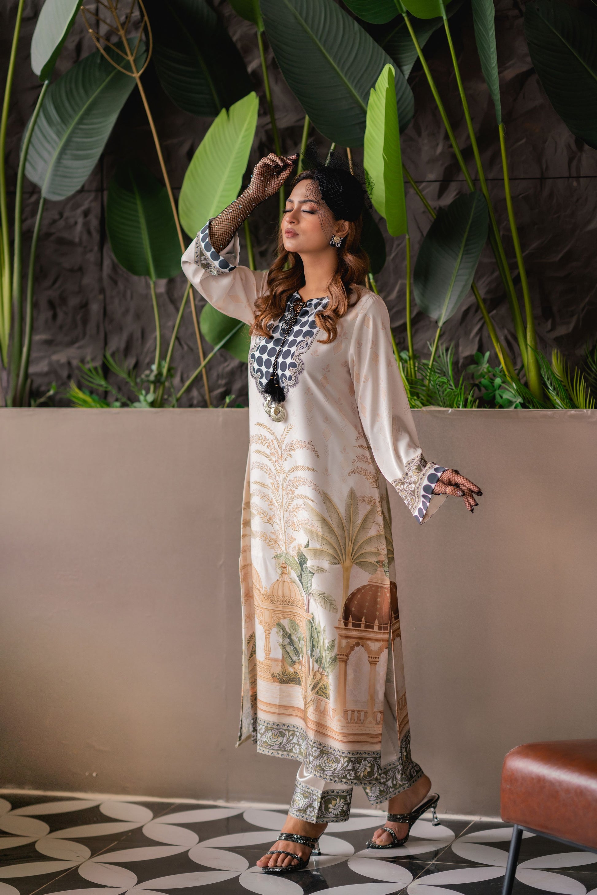 Woman in a patterned dress standing in a room with plants and a couch.