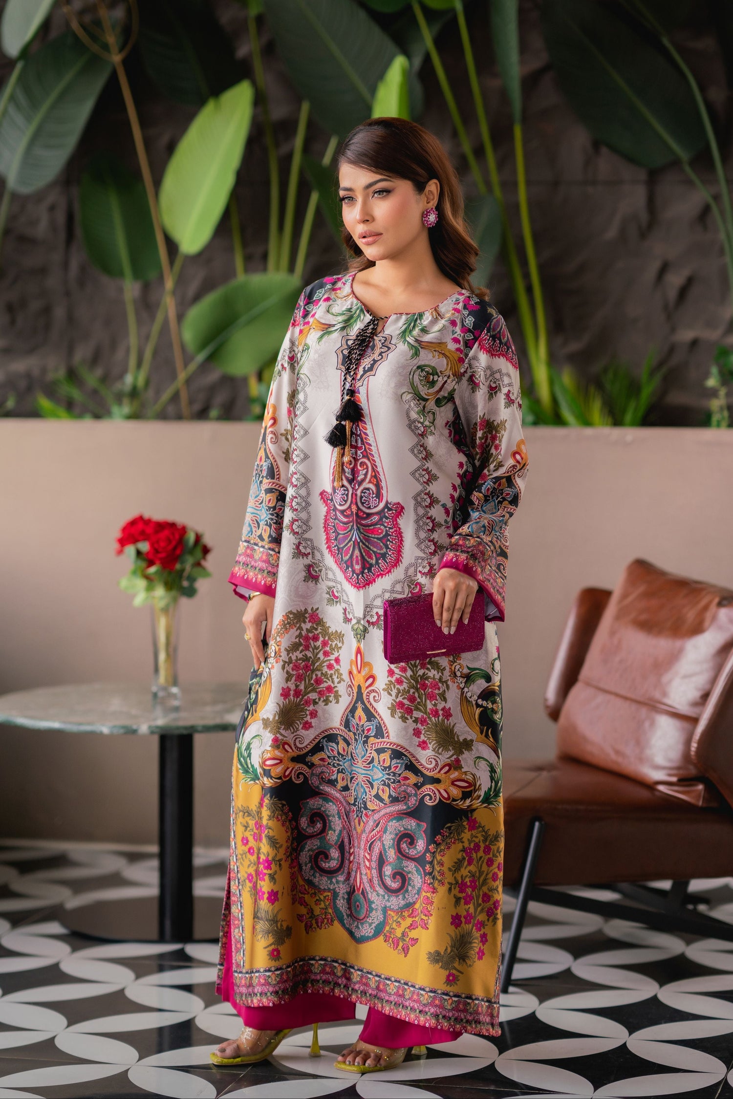 Woman in a colorful dress standing in a stylish indoor setting with plants and furniture.