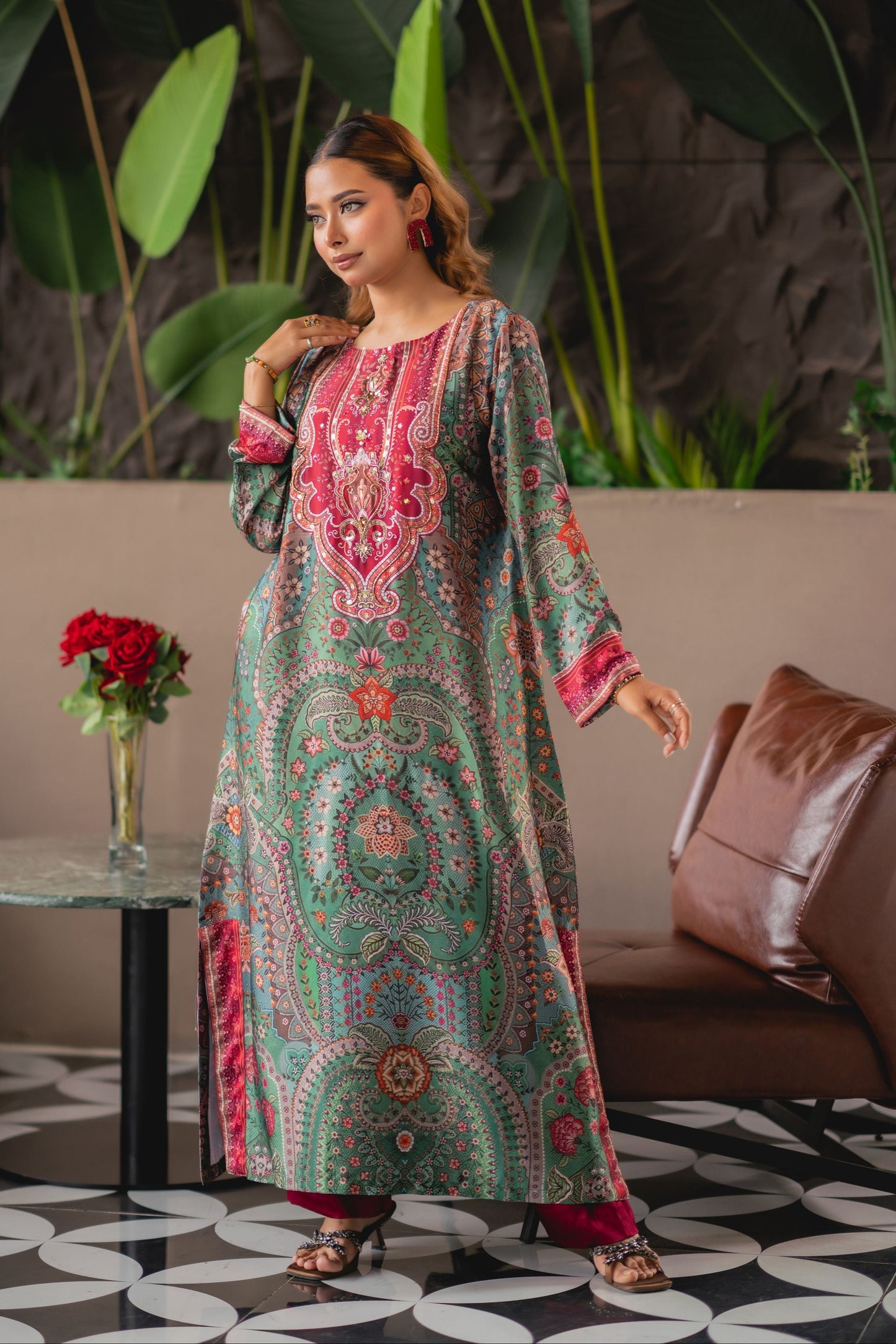 Woman in a colorful traditional outfit standing in a room with plants and a couch.