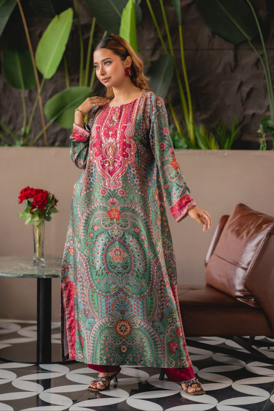 Woman in a colorful traditional outfit standing in a room with plants and a couch.