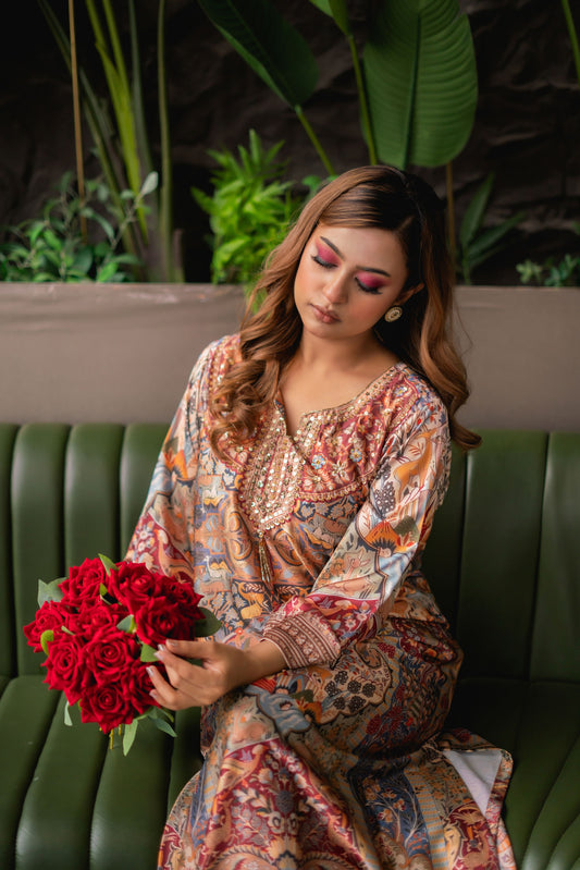Woman in a patterned dress holding red flowers, sitting on a green couch with a blurred natural background